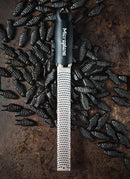 Zesteur Premium Classic Microplane on a textured surface surrounded by small black fish-shaped objects.